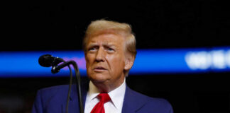 A man in a blue suit and red tie speaking into a microphone on stage