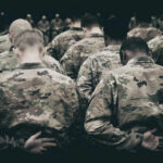 Group of soldiers in camouflage uniforms standing with heads bowed