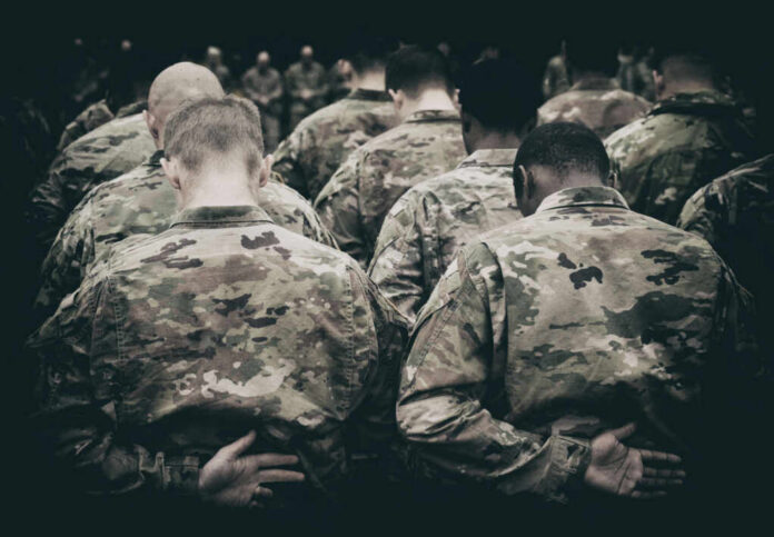 shutterstock_2380881141.jpg Group of soldiers in camouflage uniforms standing with heads bowed