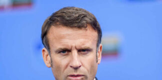 Close-up portrait of a serious-looking male political leader in formal attire against a blue background