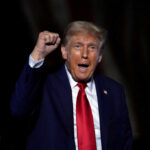 A man in a suit passionately speaking at a rally with a raised fist