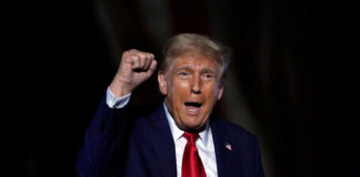 A man in a suit passionately speaking at a rally with a raised fist