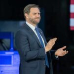 Man in a suit applauding at a political event with an American flag in the background