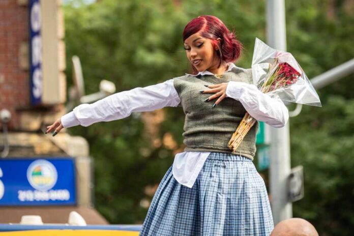 A performer in a stylish outfit holding a bouquet of flowers during a parade