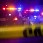 Police cars with flashing lights at a nighttime scene behind crime scene tape