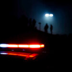 Police vehicle lights illuminating a dark scene with silhouettes in the background