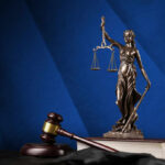 Bronze statue of Lady Justice holding scales next to a gavel on a book