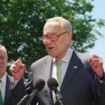 A politician speaking passionately at a press conference with microphones in front