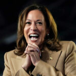 A woman in formal attire smiling broadly while speaking at a podium