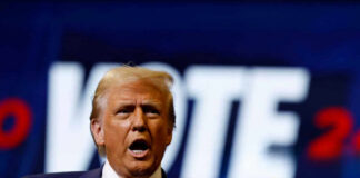 A man passionately speaking at a campaign event with a VOTE backdrop
