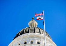 View of a state capitol dome with American and California flags against a blue sky