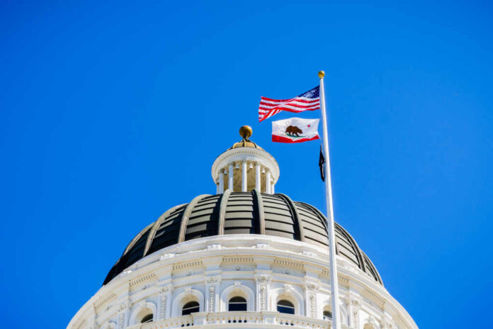 View of a state capitol dome with American and California flags against a blue sky