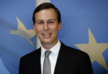 A man in a suit smiling in front of a blue background with stars
