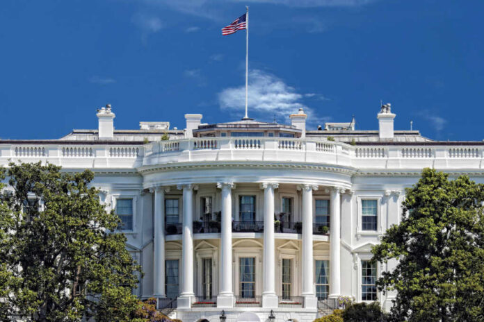 The White House with an American flag flying against a blue sky