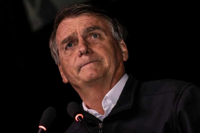 A man with a serious expression speaking into a microphone against a dark background