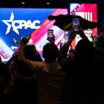 Audience members at a CPAC event holding phones and flags