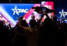 Audience members at a CPAC event holding phones and flags