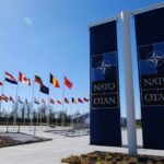 Flags of various nations displayed outside NATO headquarters under a clear blue sky