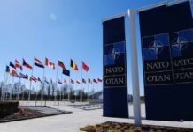 Trump BLASTS NATO: “Cowards” Over Strait Security Flags of various nations displayed outside NATO headquarters under a clear blue sky