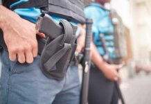 Two security personnel in tactical gear, one with a visible firearm
