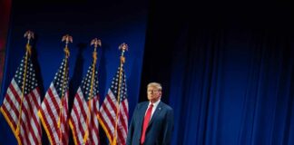 A man in a suit standing on stage next to American flags