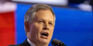 A man in a suit speaking passionately into a microphone at a political event
