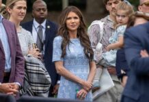 A group of people at an outdoor event, with a woman in a blue dress standing in the foreground