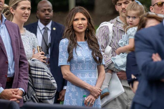 shutterstock_2616120153.jpg A group of people at an outdoor event, with a woman in a blue dress standing in the foreground