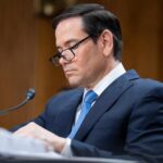 Individual in a suit reviewing documents during a senate hearing