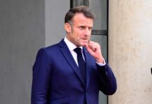Emmanuel Macron in a suit, standing outdoors with a thoughtful expression