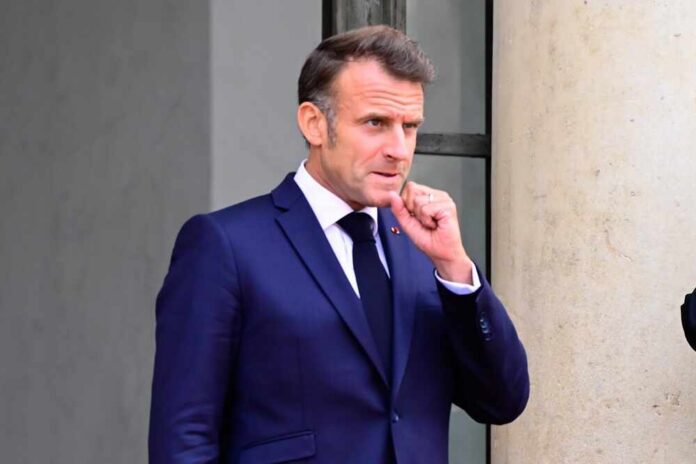 Emmanuel Macron in a suit, standing outdoors with a thoughtful expression