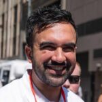 A smiling man in a casual white shirt standing outdoors