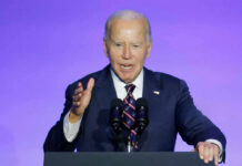 A man in a suit speaking at a podium with microphones against a blue background