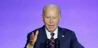 A man in a suit speaking at a podium with microphones against a blue background