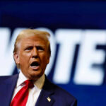 A man passionately speaking at a campaign event with a VOTE backdrop
