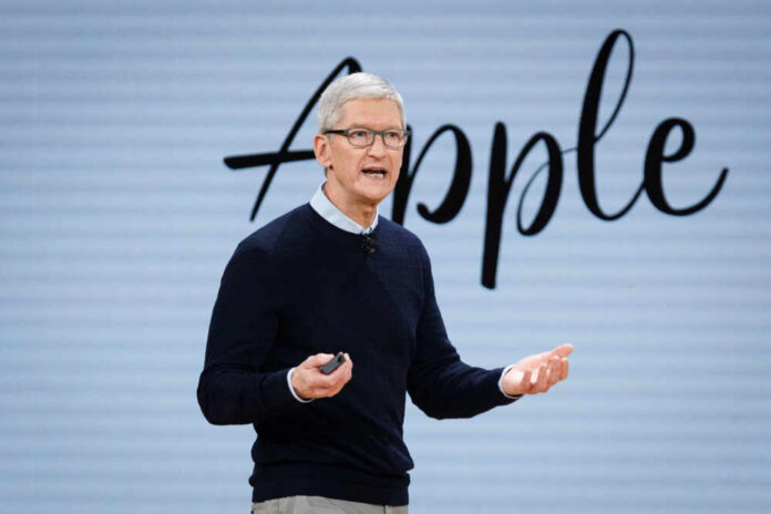 A speaker presenting at a corporate event with an Apple logo in the background