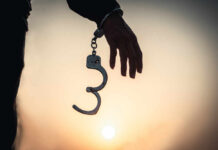 Silhouette of a hand holding handcuffs against a sunset