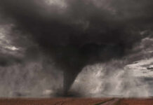 A tornado forming in a dark, stormy sky over a field