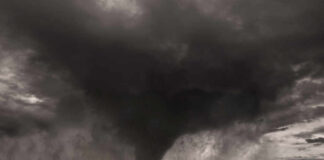 A tornado forming in a dark, stormy sky over a field