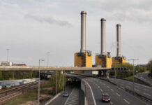 Industrial power plant with three tall smokestacks beside a highway