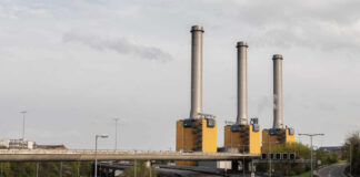 Industrial power plant with three tall smokestacks beside a highway