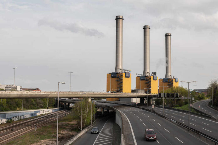 Industrial power plant with three tall smokestacks beside a highway