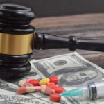 A gavel placed on top of money with pills and a syringe nearby