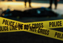Yellow police caution tape at a crime scene with blurred figures in the background