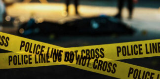 Yellow police caution tape at a crime scene with blurred figures in the background