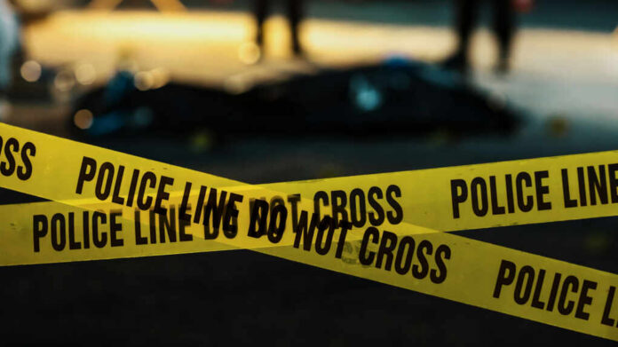 Yellow police caution tape at a crime scene with blurred figures in the background