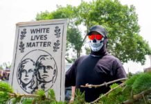 Neo-Nazi Combat Training Exposed in Virginia Individual holding a sign that reads 'White Lives Matter' while wearing a skull mask