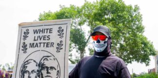 Neo-Nazi Combat Training Exposed in Virginia Individual holding a sign that reads 'White Lives Matter' while wearing a skull mask