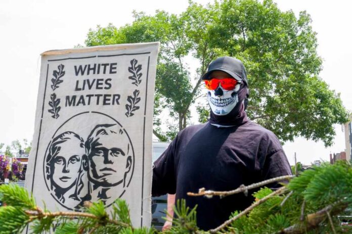 Individual holding a sign that reads 'White Lives Matter' while wearing a skull mask