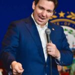 A man in a blue suit speaking into a microphone at a public event